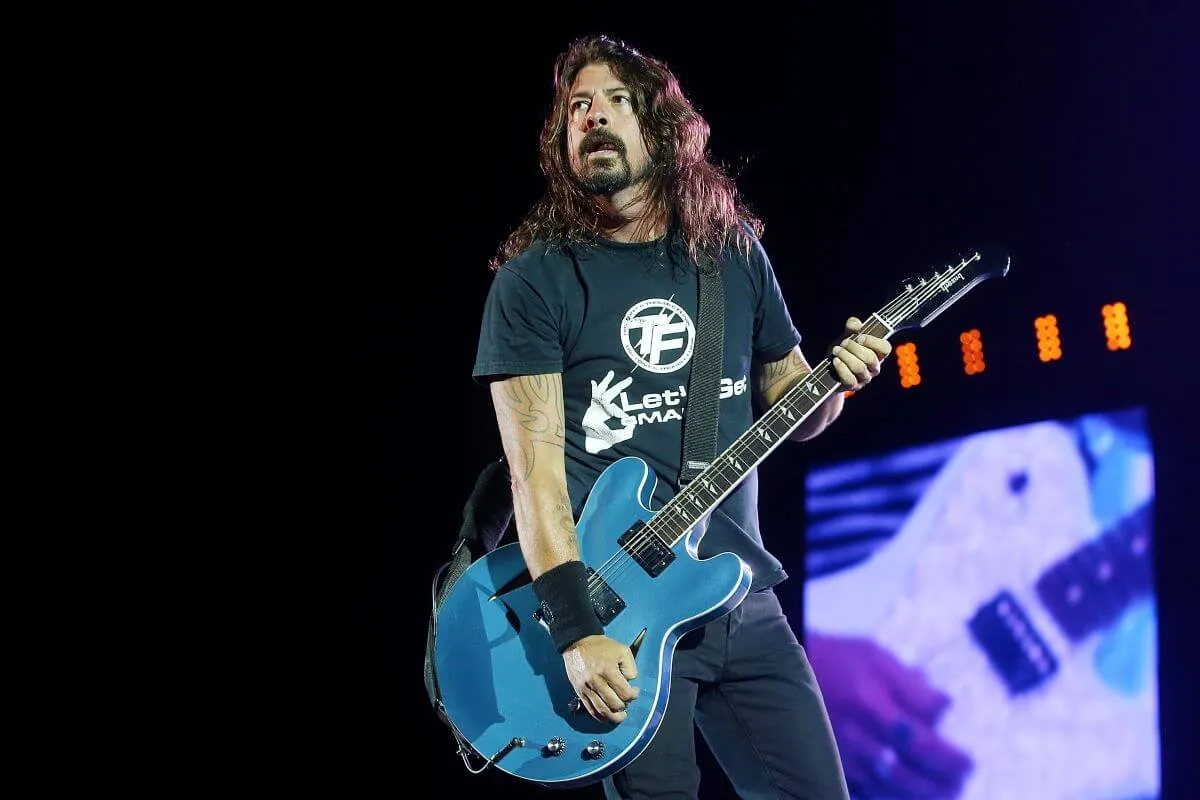 Dave Grohl wears a t shirt and strums an electric guitar.