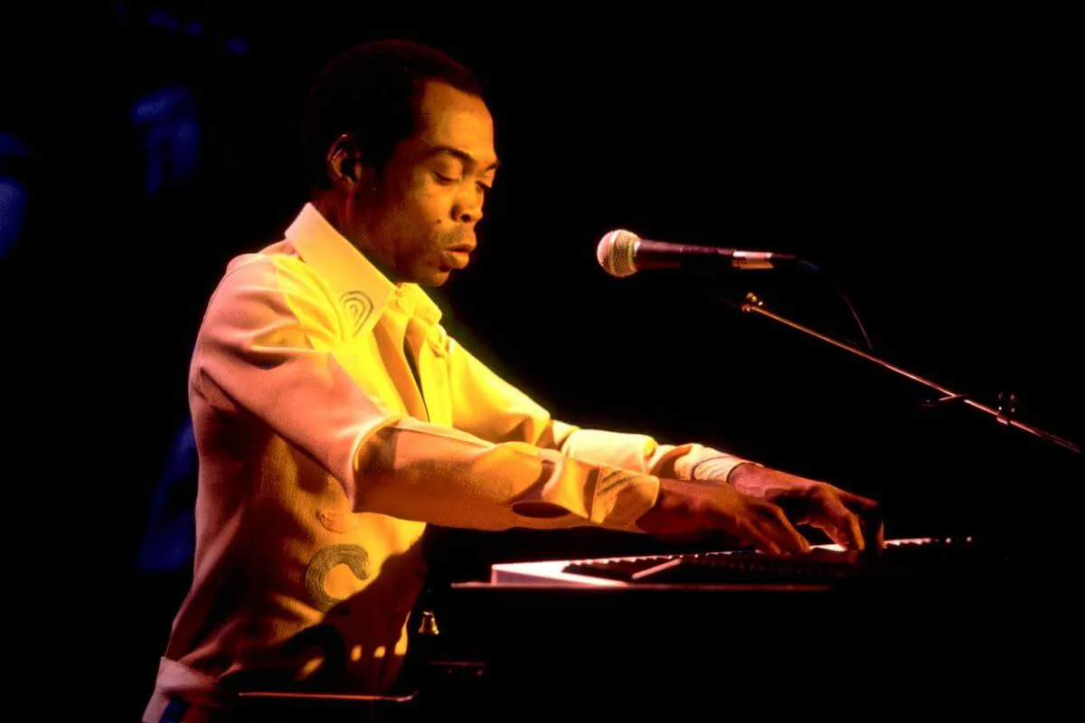 Fela Kuti wears a white shirt and plays piano.