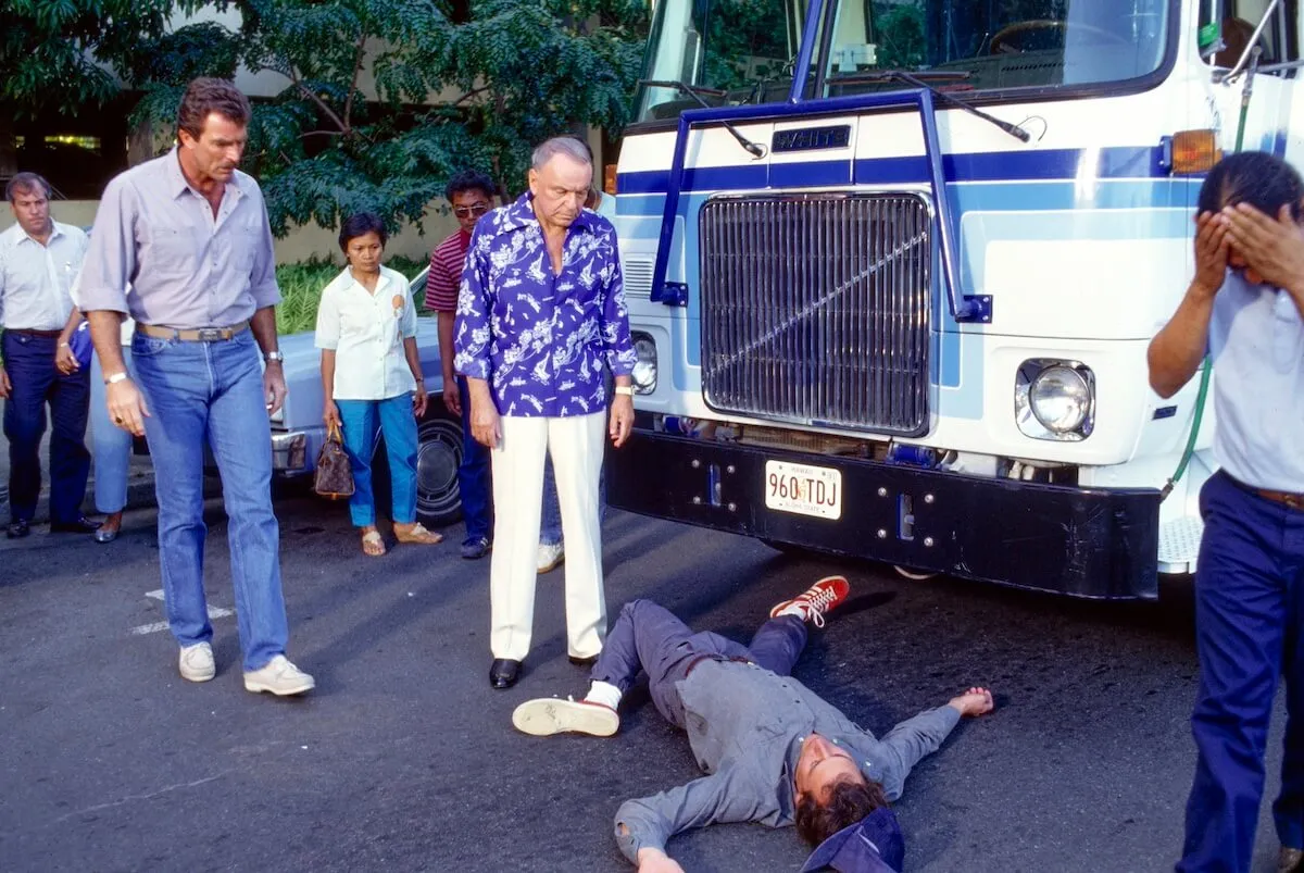 Frank Sinatra wearing a Hawaiian-print shirt and looking at a man on the ground on the set of 'Magnum P.I.'