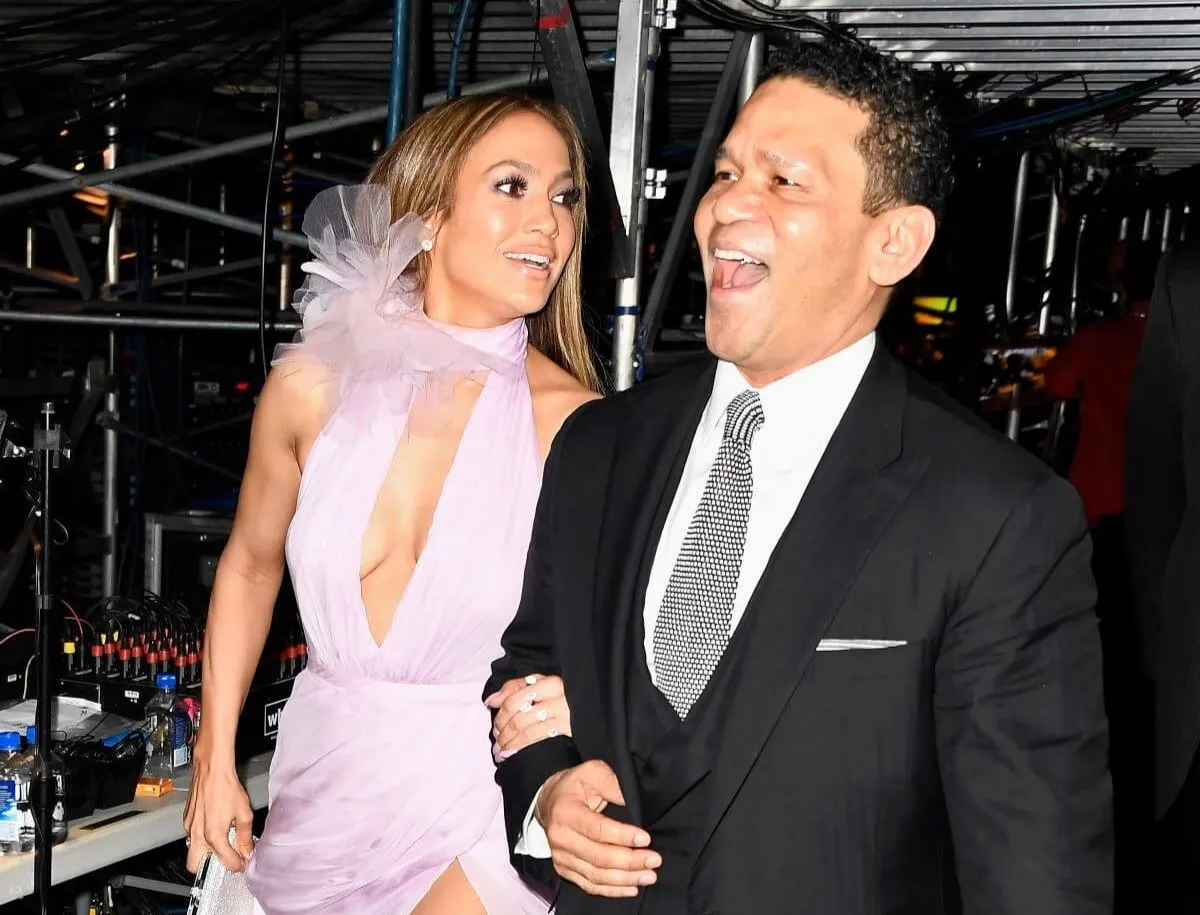 Jennifer Lopez wears a lavender dress and walks arm in arm with her manager, Benny Medina. He wears a suit.