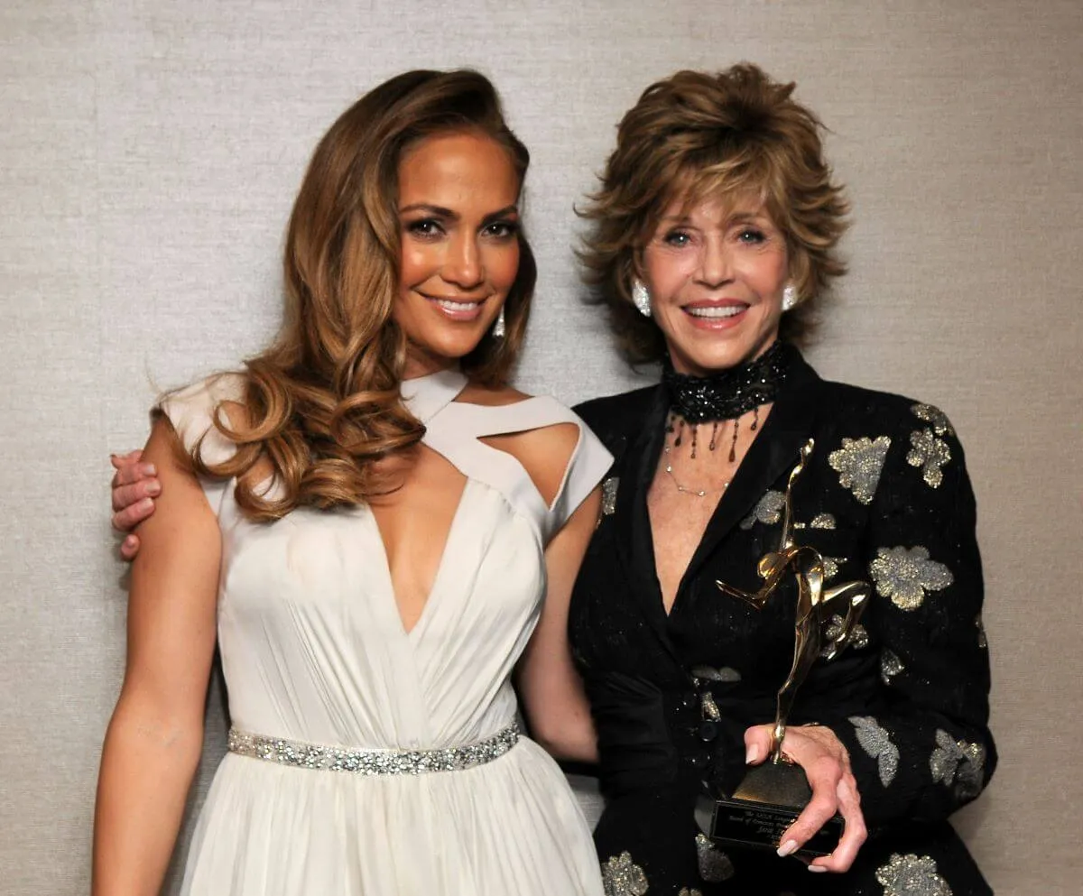 Jennifer Lopez wears a white dress and stands with Jane Fonda, who wears a black dress.