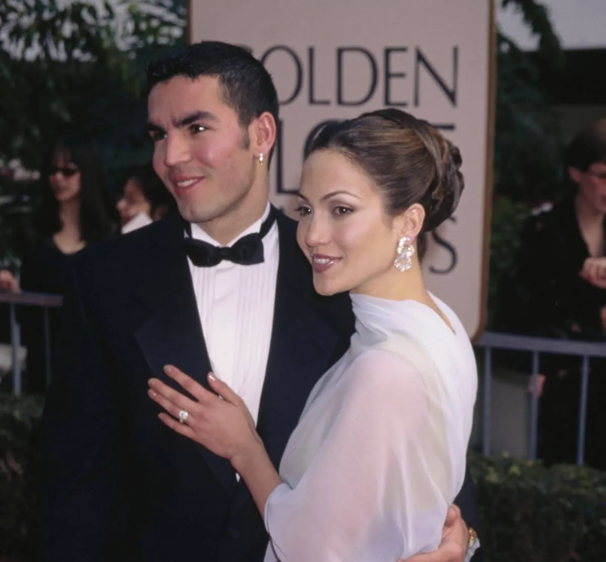 Jennifer Lopez wears a shawl and stands with her hand on her husband Ojani Noa's chest. He wears a tuxedo.