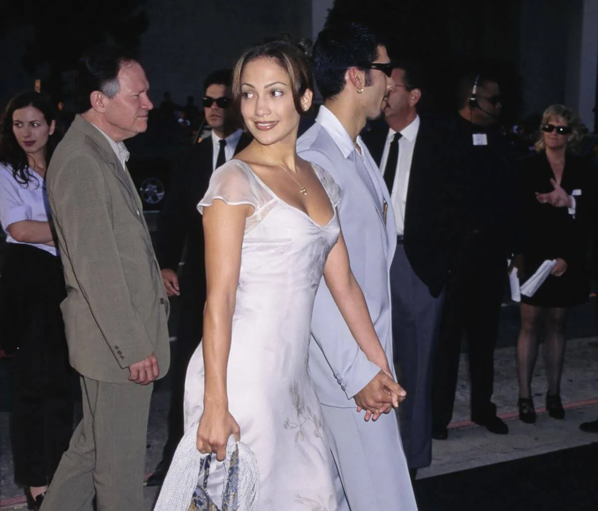 Jennifer Lopez wears a white dress and holds hands with her husband, Ojani Noa, on the red carpet.