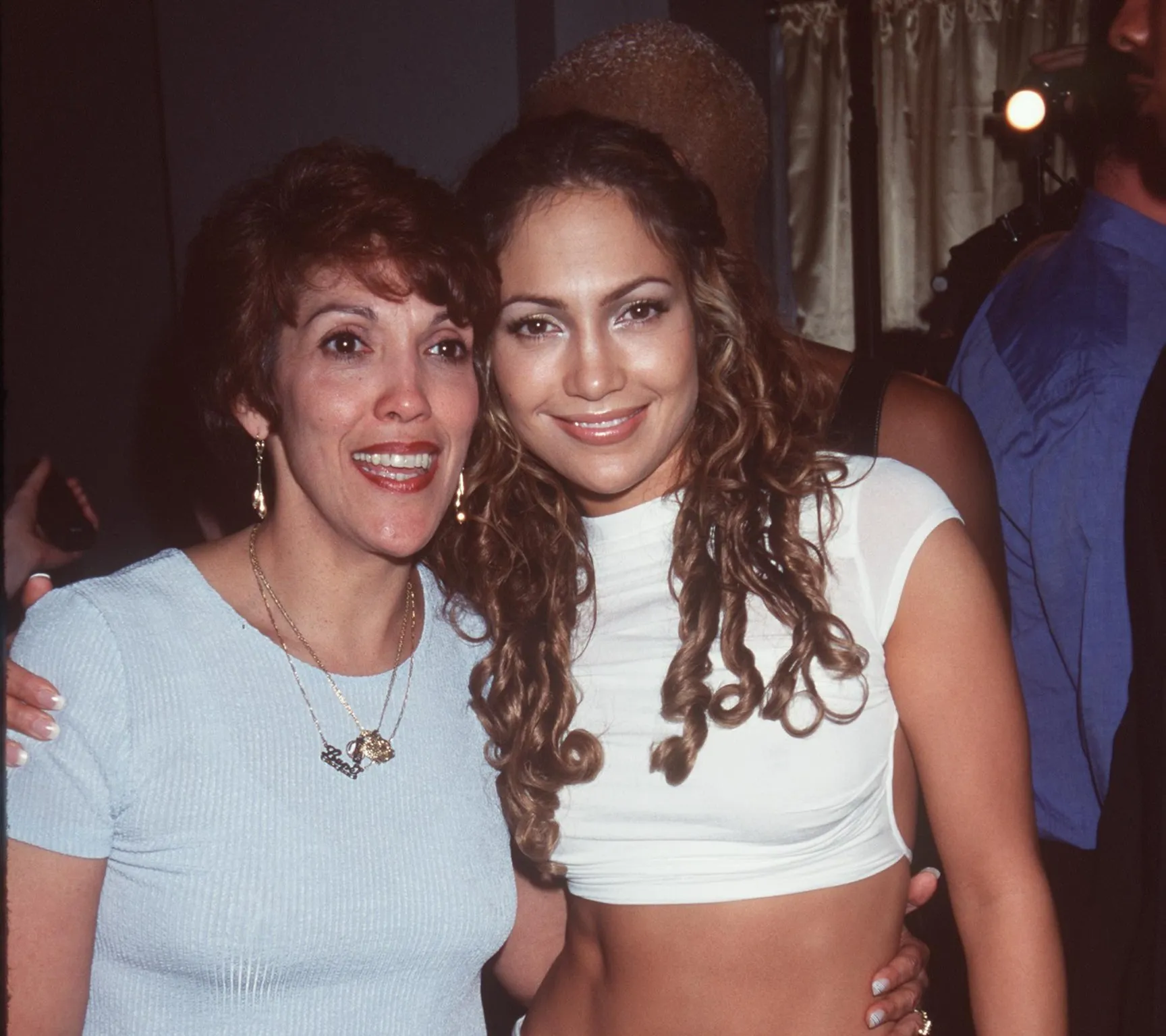 Jennifer Lopez wears a white cropped shirt and stands with her arm around her mom.