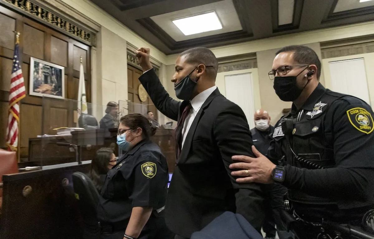 Wearing a black suit, Jussie Smollett raises his hand in court in Chicago