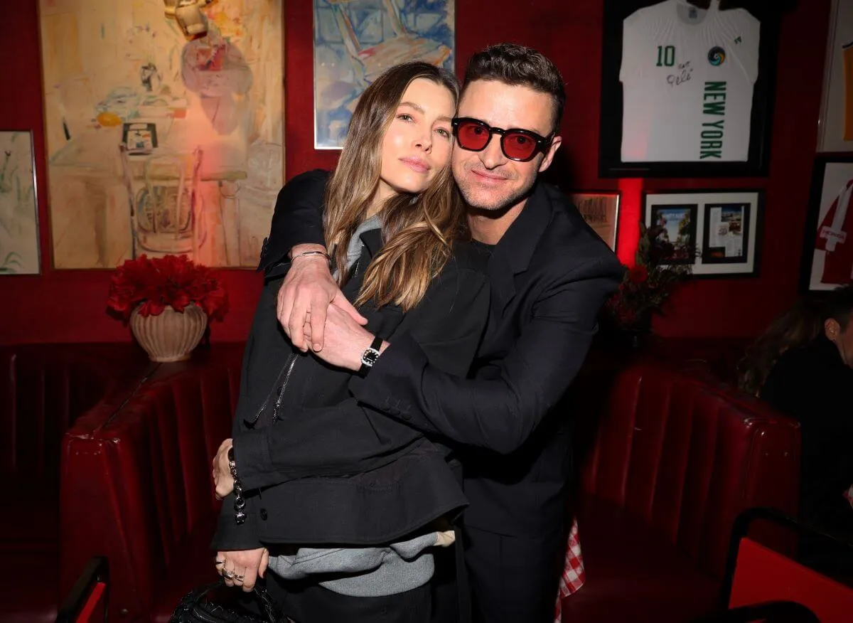 Justin Timberlake wears red tinted sunglasses and embraces Jessica Biel from behind.