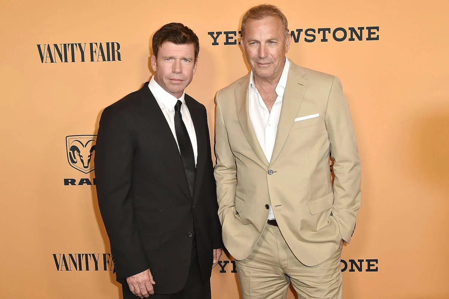 Kevin Costner and Taylor Sheridan standing next to each other against a yellow-gold background at the 'Yellowstone' premiere