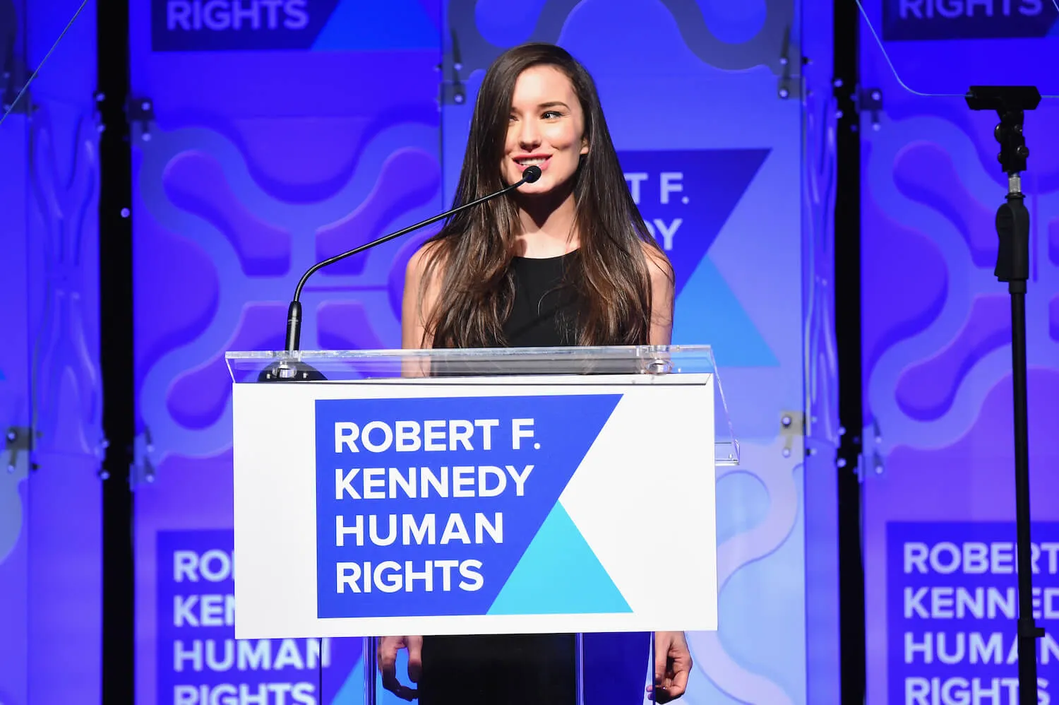 Kick Kennedy against a blue background while speaking at a podium for RFK Human Rights Ripple of Hope Awards