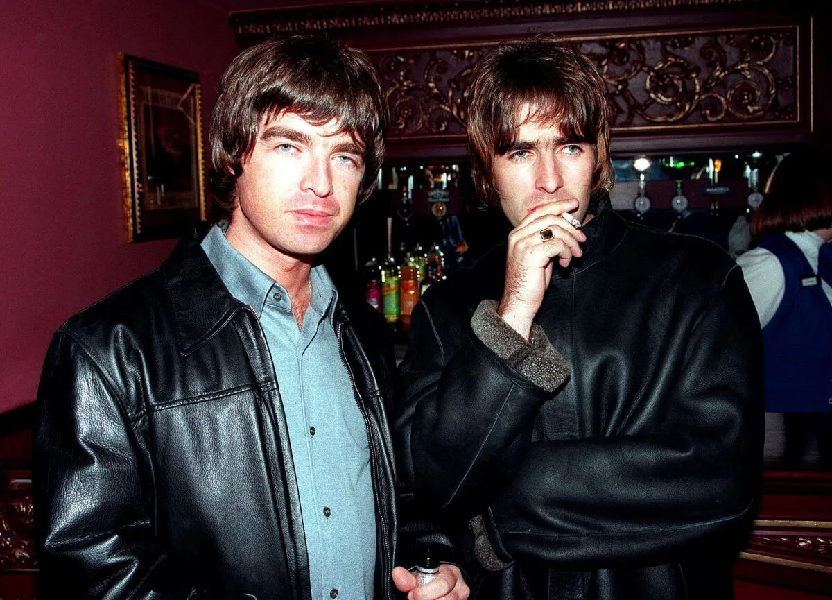 Noel Gallagher and his brother, Liam Gallagher, stand together. They both wear black leather jackets.