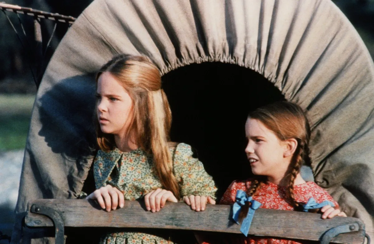 Mary and Laura Ingalls riding in a covered wagon in 'Little House on the Prairie'