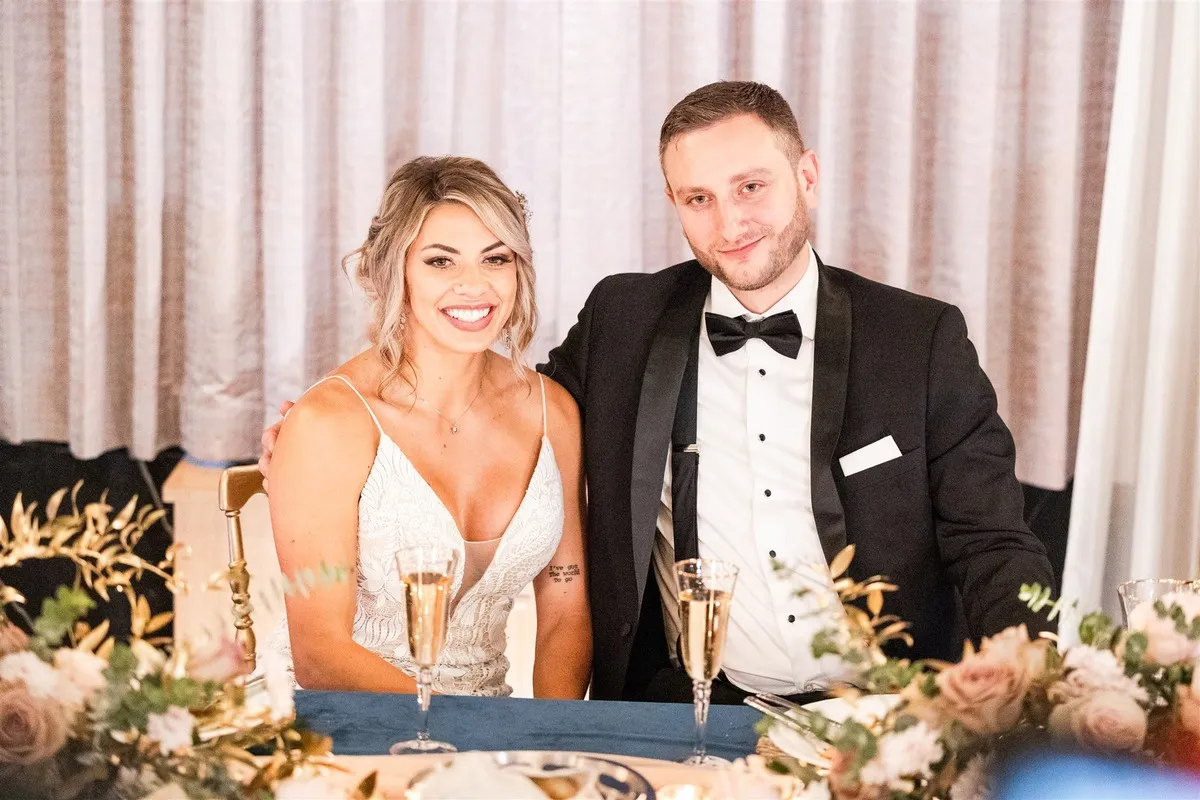 Man and woman smile for a photo on their wedding day while sitting at a table