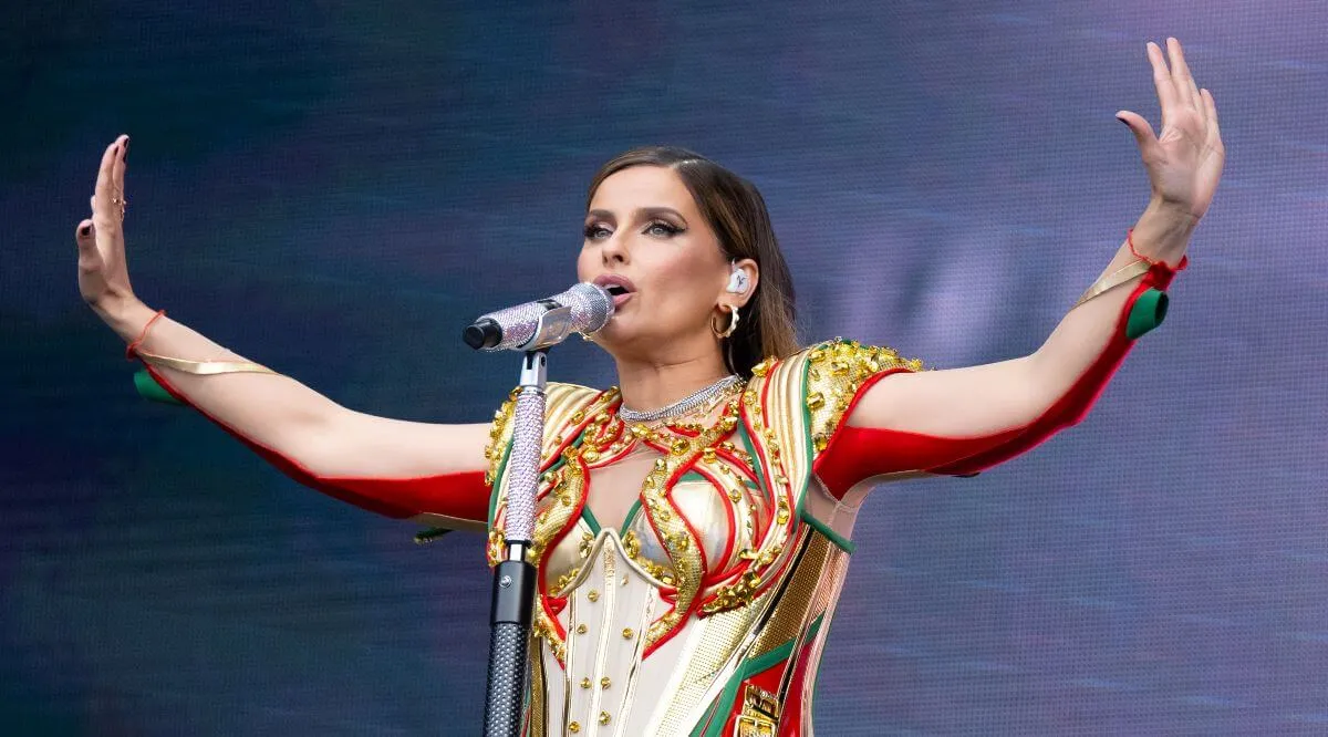 Nelly Furtado wears a gold, green, and red shirt and sings into a microphone.