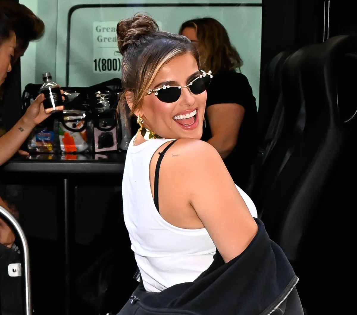 Nelly Furtado wears a white tank top and sunglasses. She looks over her shoulder.