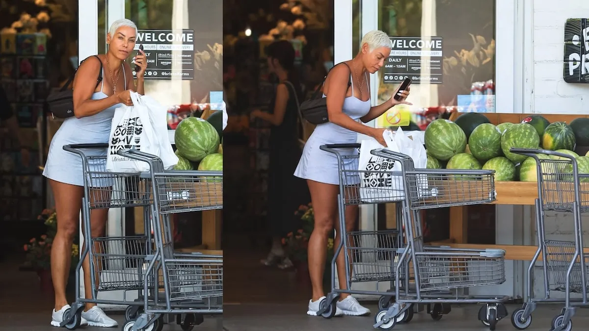 Wearing a blue tennis dress, Nicole Mitchell exits a grocery store carrying two grocery bags and talking on her cell phone