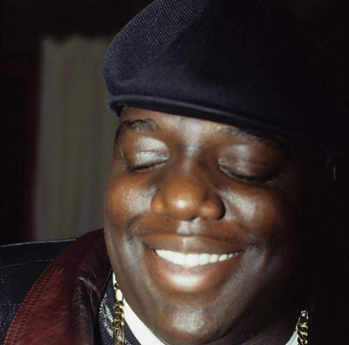 The Notorious B.I.G. wears a hat and smiles.