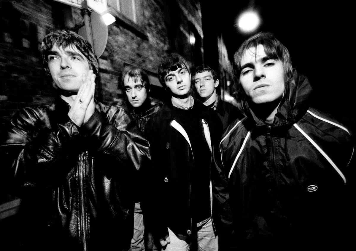 A black and white picture of Oasis posing outside a brick building.