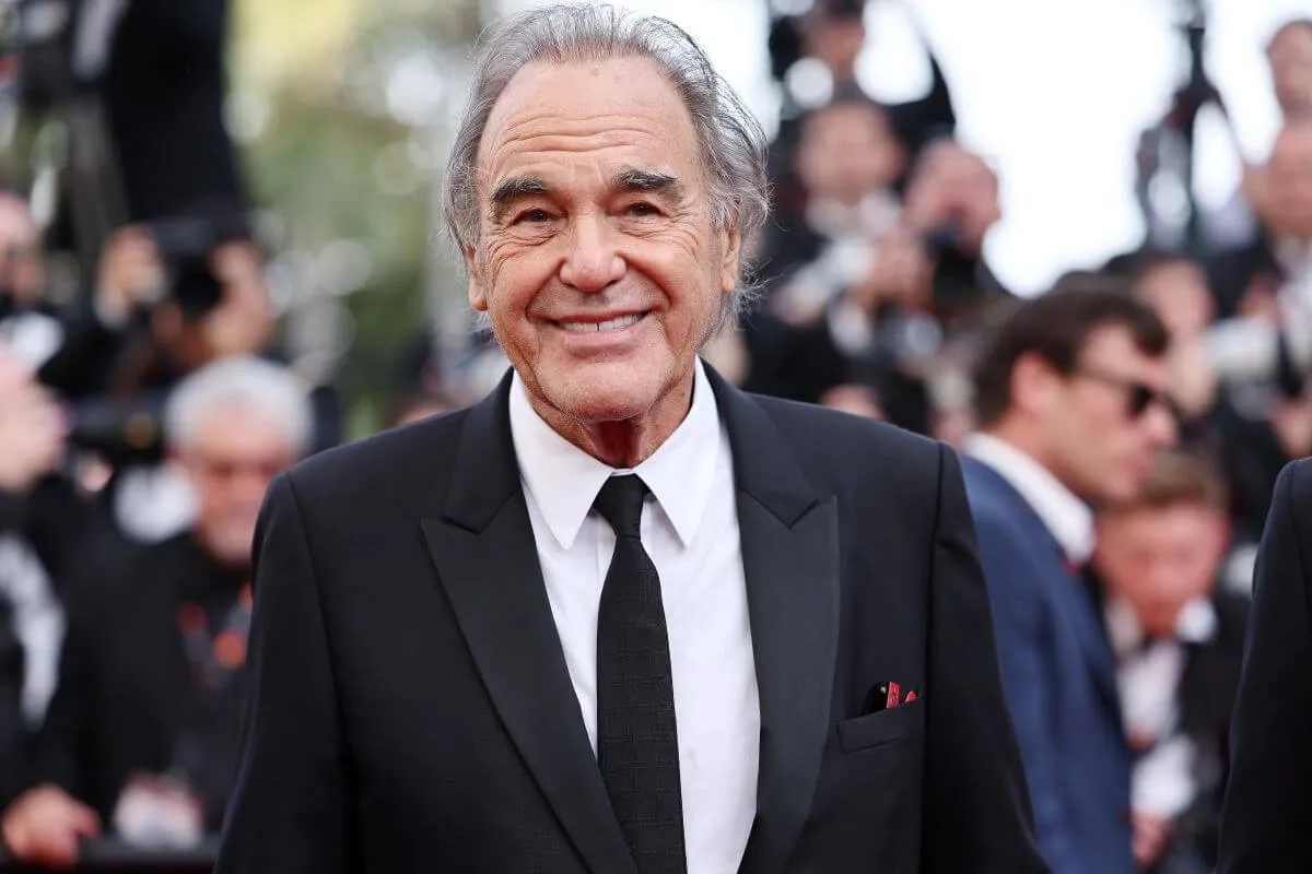 Oliver Stone wears a suit and stands on the red carpet.