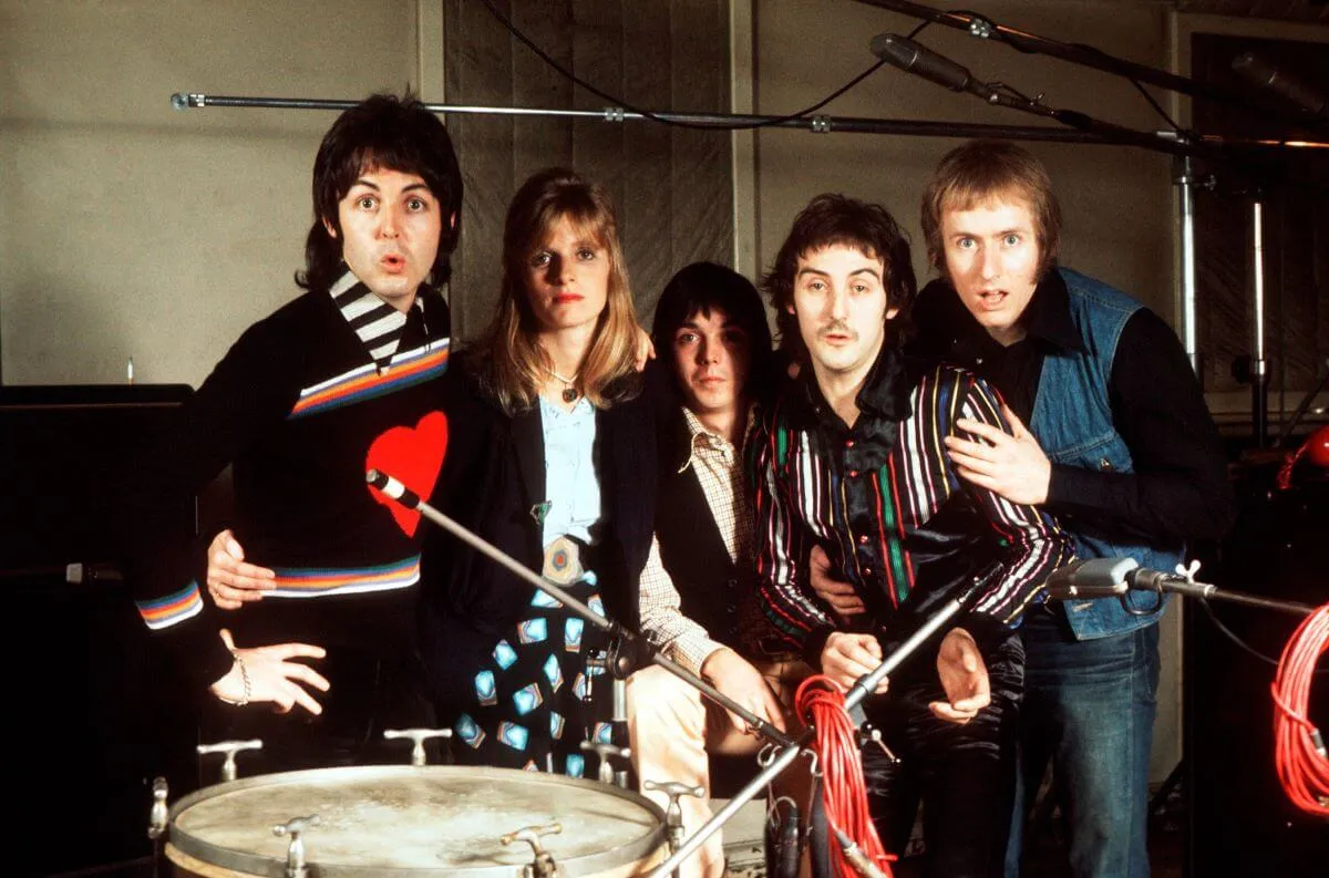 Paul McCartney stands in a row with his band Wings. They pose near a drum.