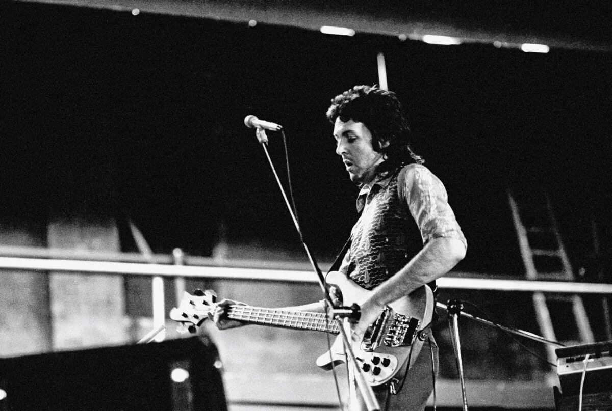 A black and white picture of Paul McCartney holding a guitar and standing behind a microphone.