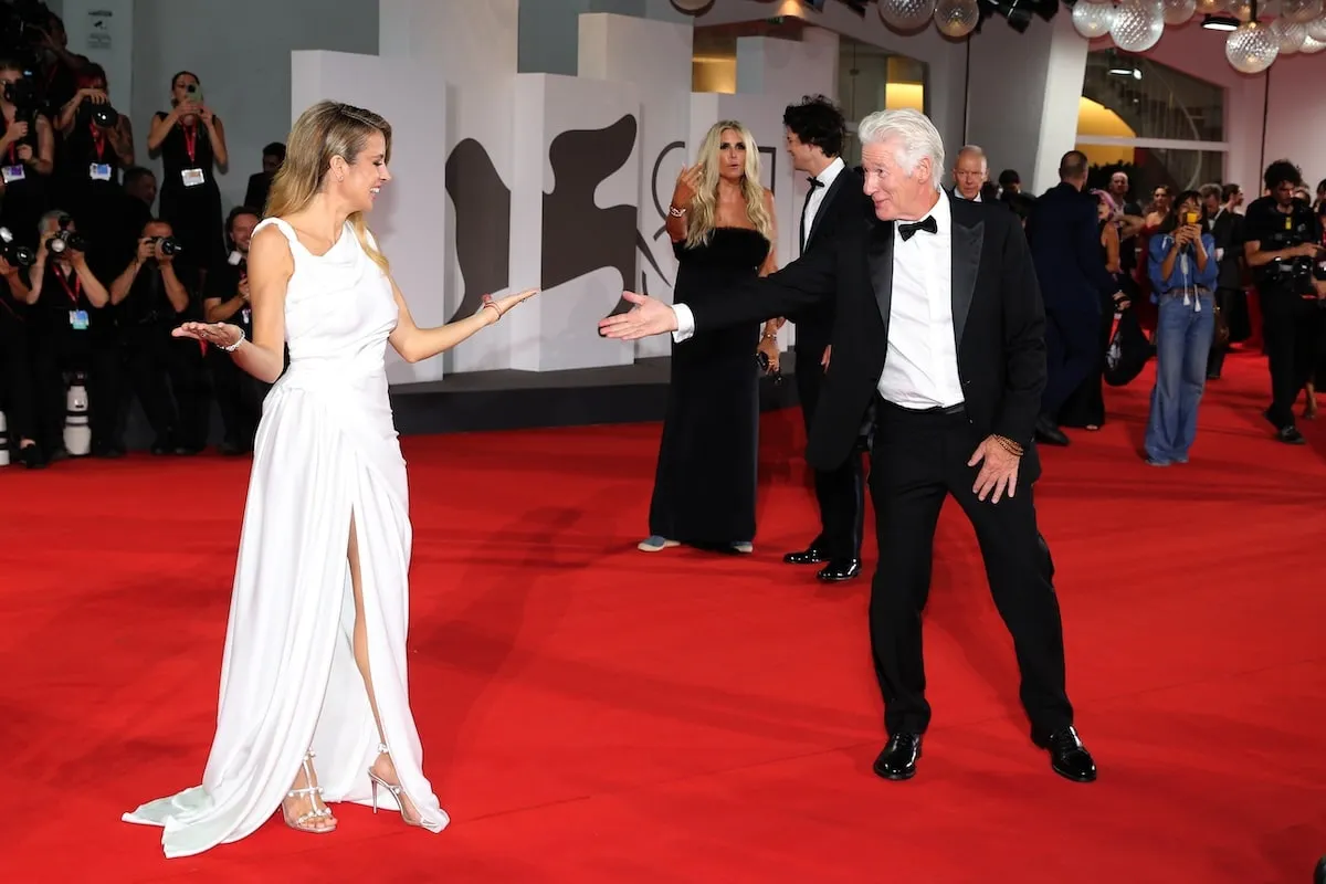 Wearing a tuxedo, Richard Gere holds his wife Alejandra Silva's hand as they attend the Filming Italy Venice Award red carpet