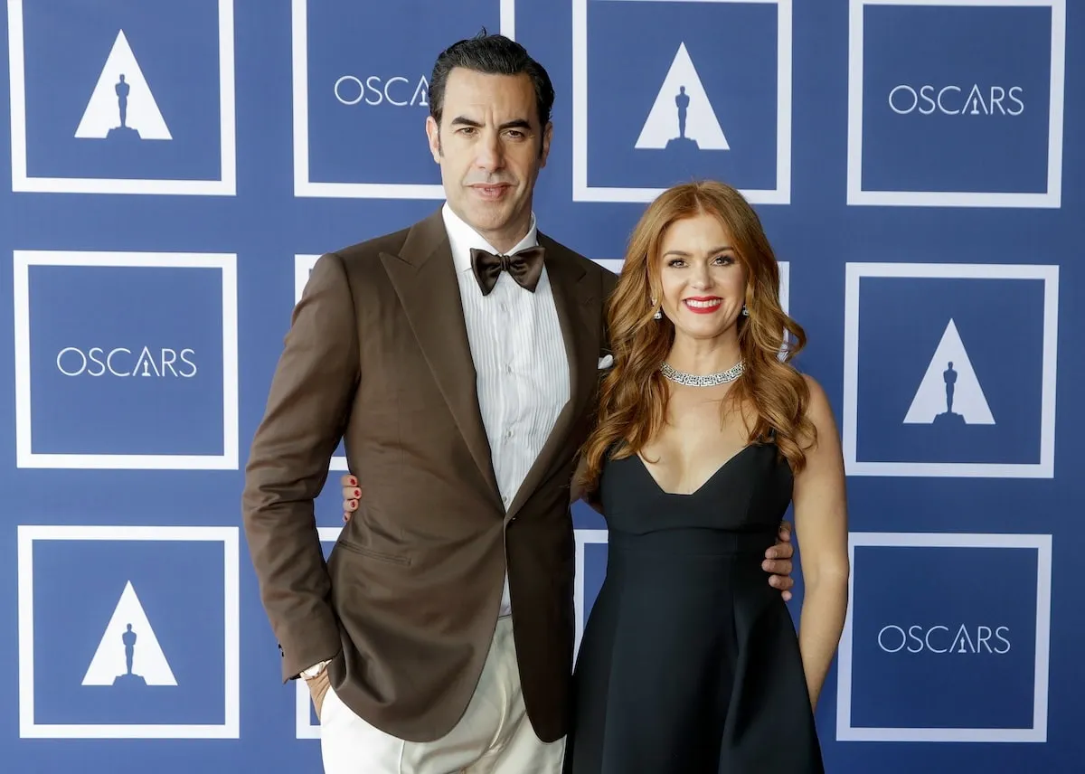 Wearing a brown suit and navy dress, Sacha Baron Cohen and Isla Fisher attend a screening of the Oscars in 2021