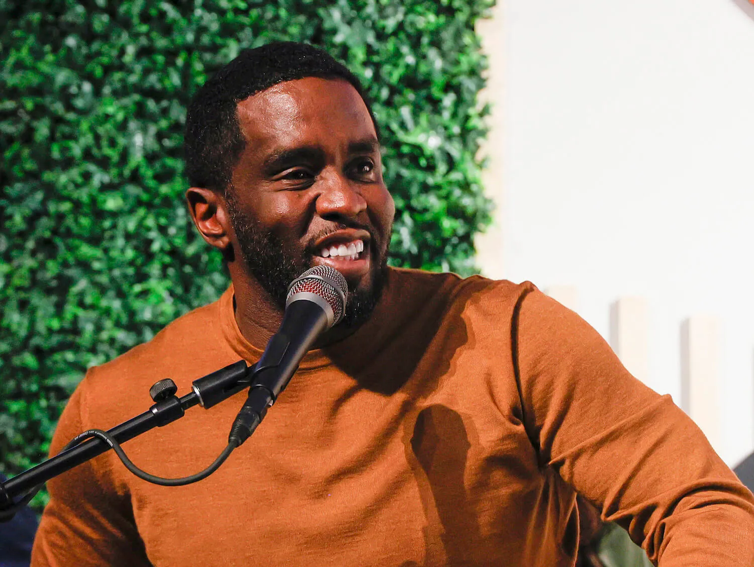 Sean 'P. Diddy' Combs wearing a burnt orange shirt and smiling while speaking into a microphone