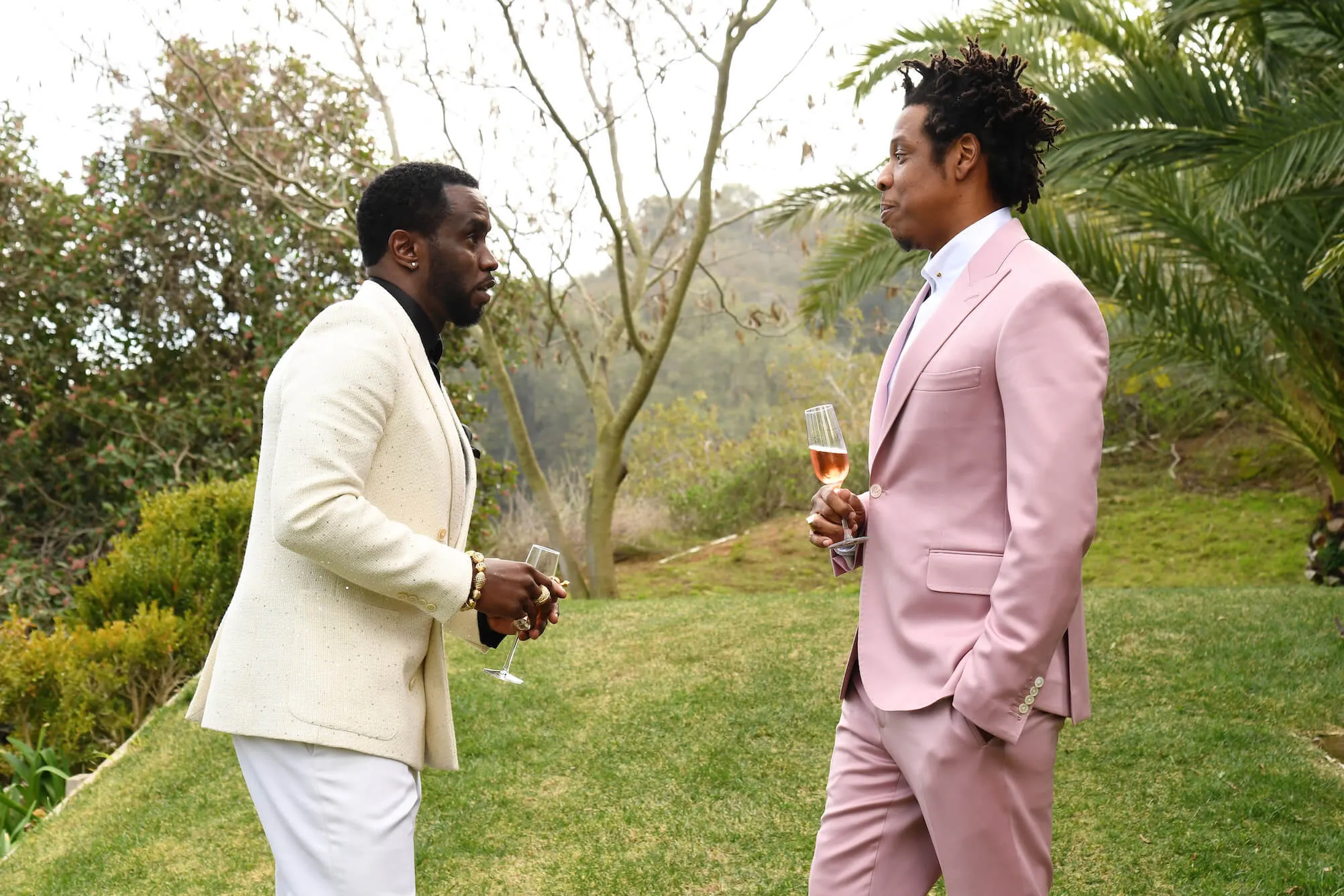 Sean 'P. Diddy' Combs wearing a light yellow suit jacked while talking to Jay-Z, who's wearing a pink suit. They're outside.