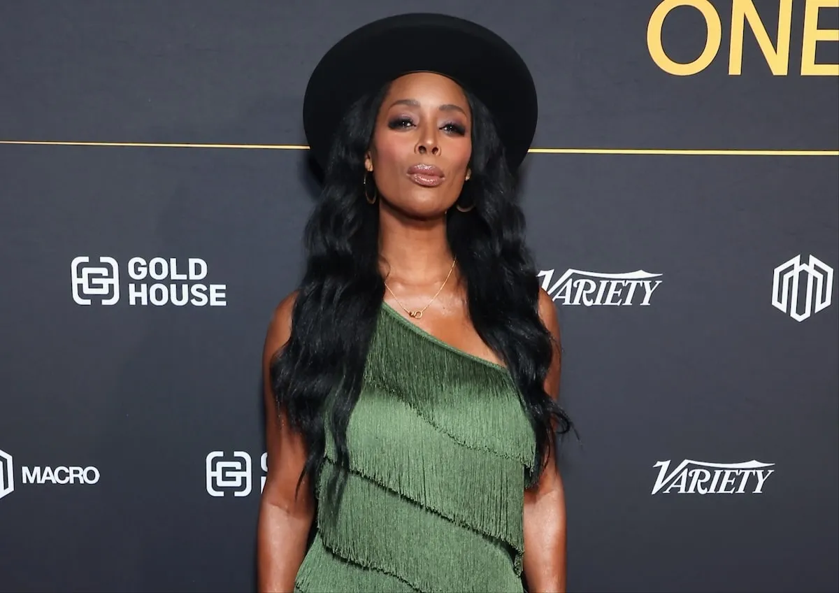 Wearing a green fringed dress, Tasha Smith stands on a red carpet in 2024