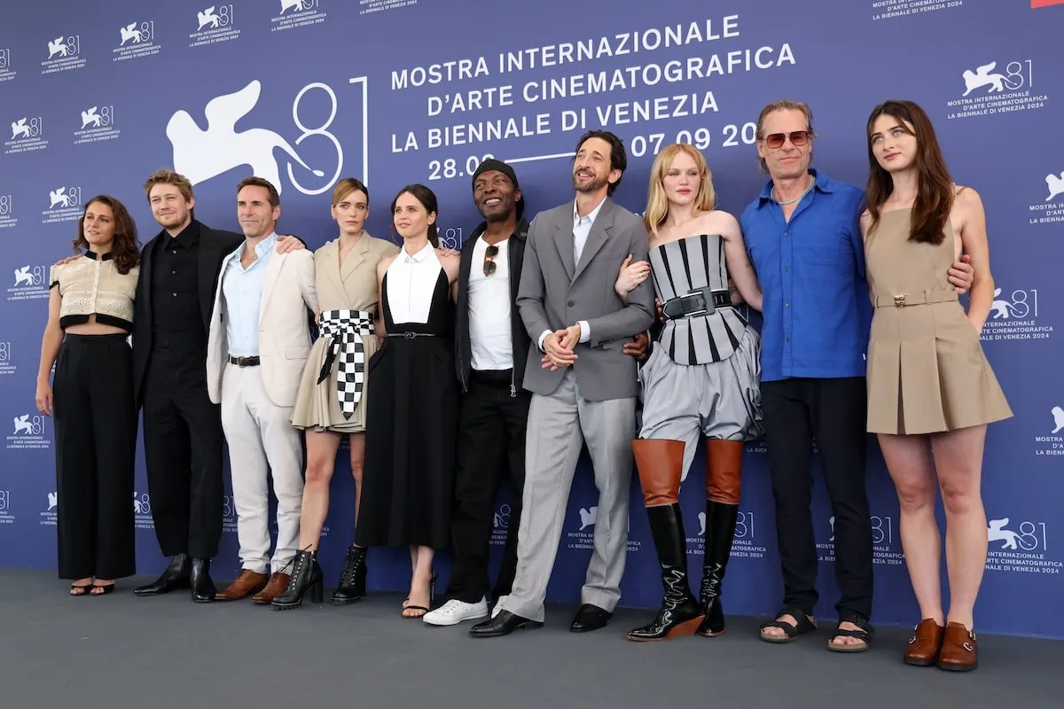 The cast of The Brutalist gather for a photo at the Venice Film Festival in front of a purple wall