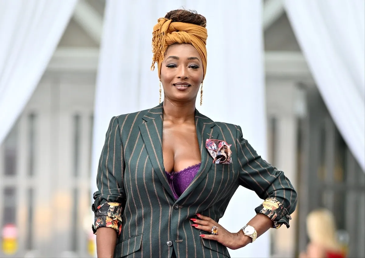 Model Toccara Jones poses on purple carpet while wearing a gray suit and purple bra in 2024