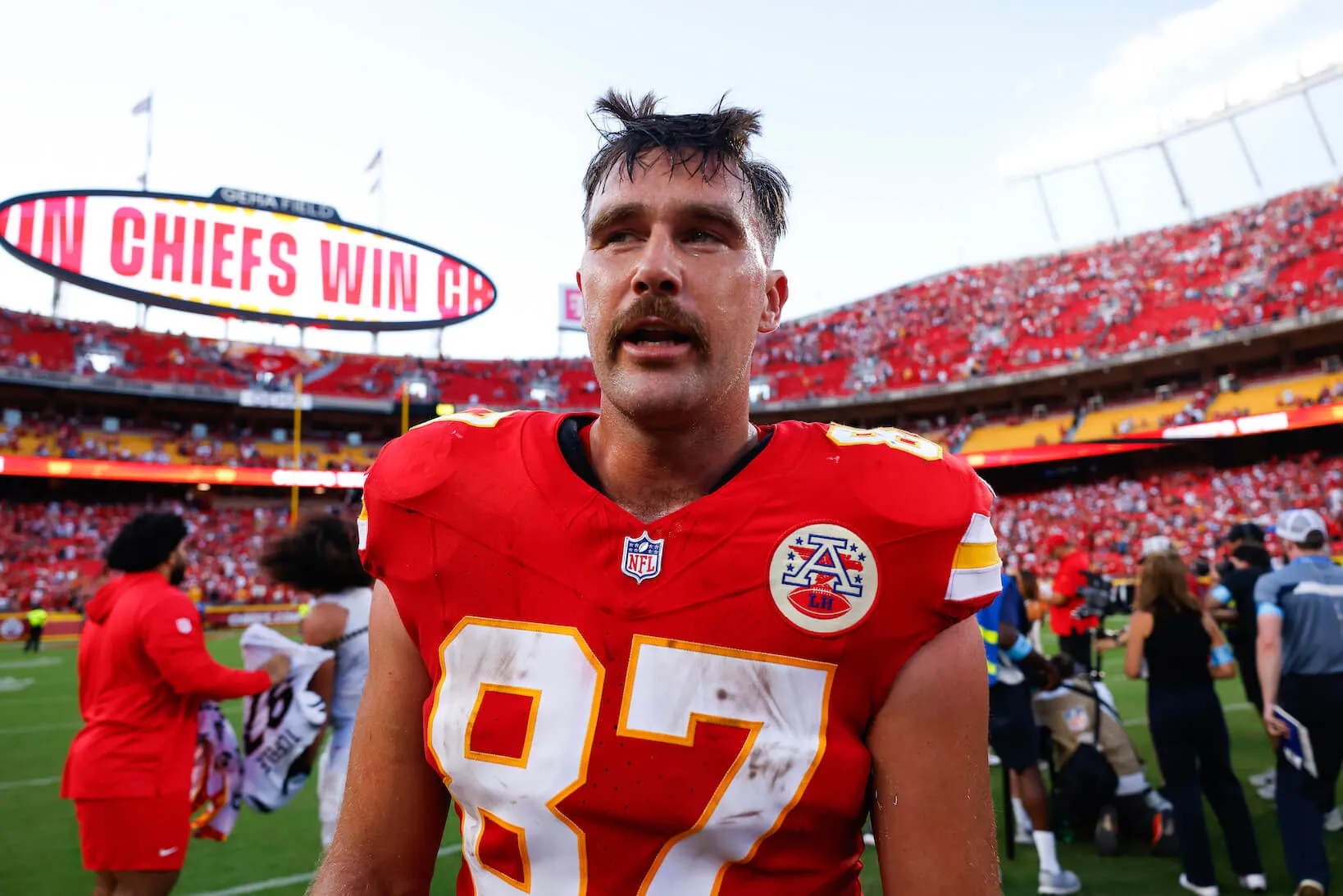 Travis Kelce sweating while on the field playing for the Kansas City Chiefs. The stadium is in the background.