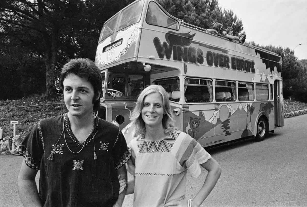 A black and white picture of Paul and Linda McCartney standing in front of the Wings tour bus.