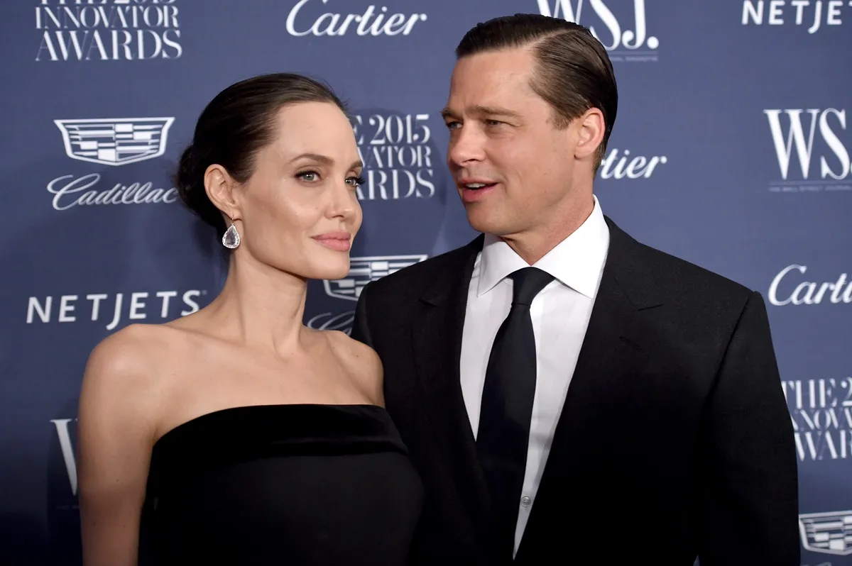 Angelina Jolie posing in a black dress next to Brad Pitt at the WSJ. Magazine 2015 Innovator Awards.