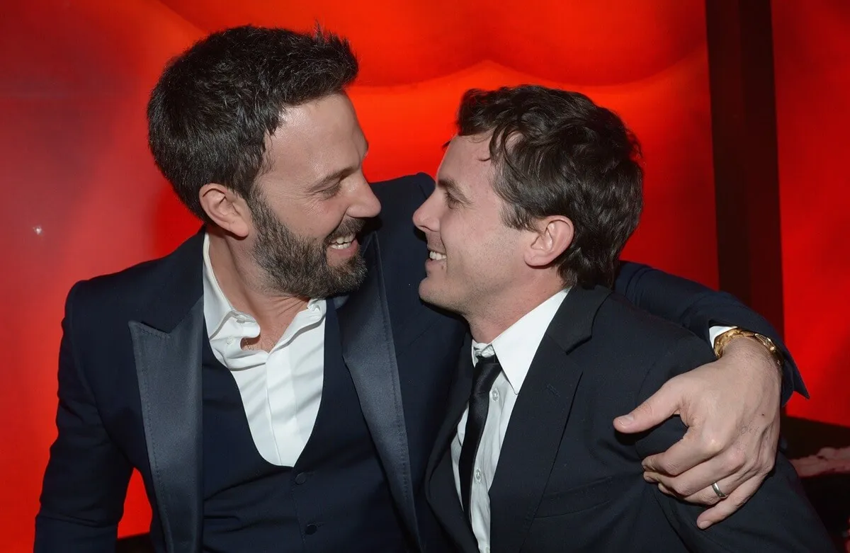 Casey Affleck wearing a suit while smiling next to Ben Affleck at the 2013 InStyle and Warner Bros. 70th Annual Golden Globe Awards.