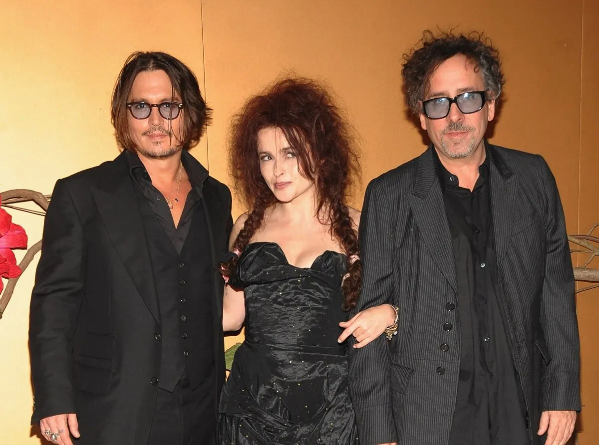 Helena Bonham Carter posing between Johnny Depp and Tim Burton while they all wear matching-colored black outfits.