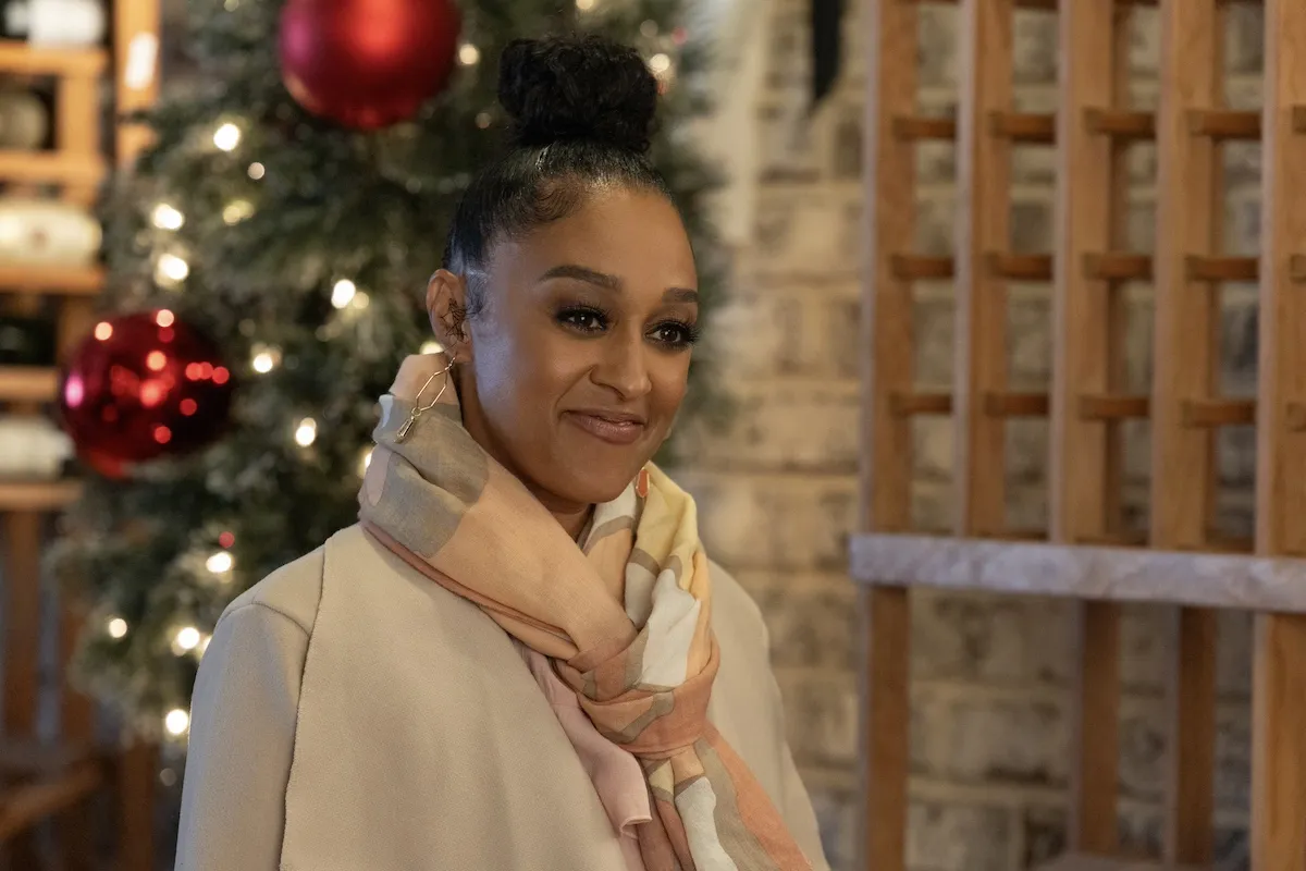 Tia Mowry wearing a scarf and standing in front of a Christmas tree