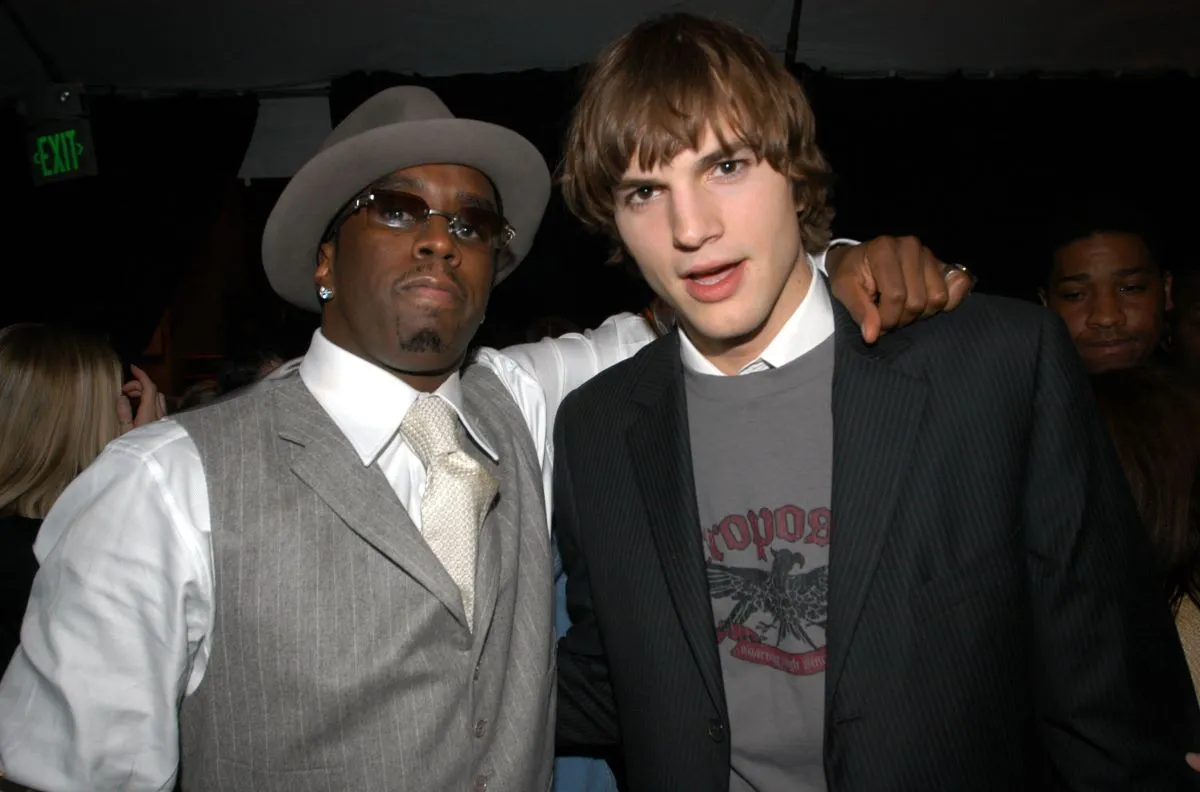 Sean "Diddy" Combs wears a tie, hat, and sunglasses and has his arm around Ashton Kutcher's shoulders.