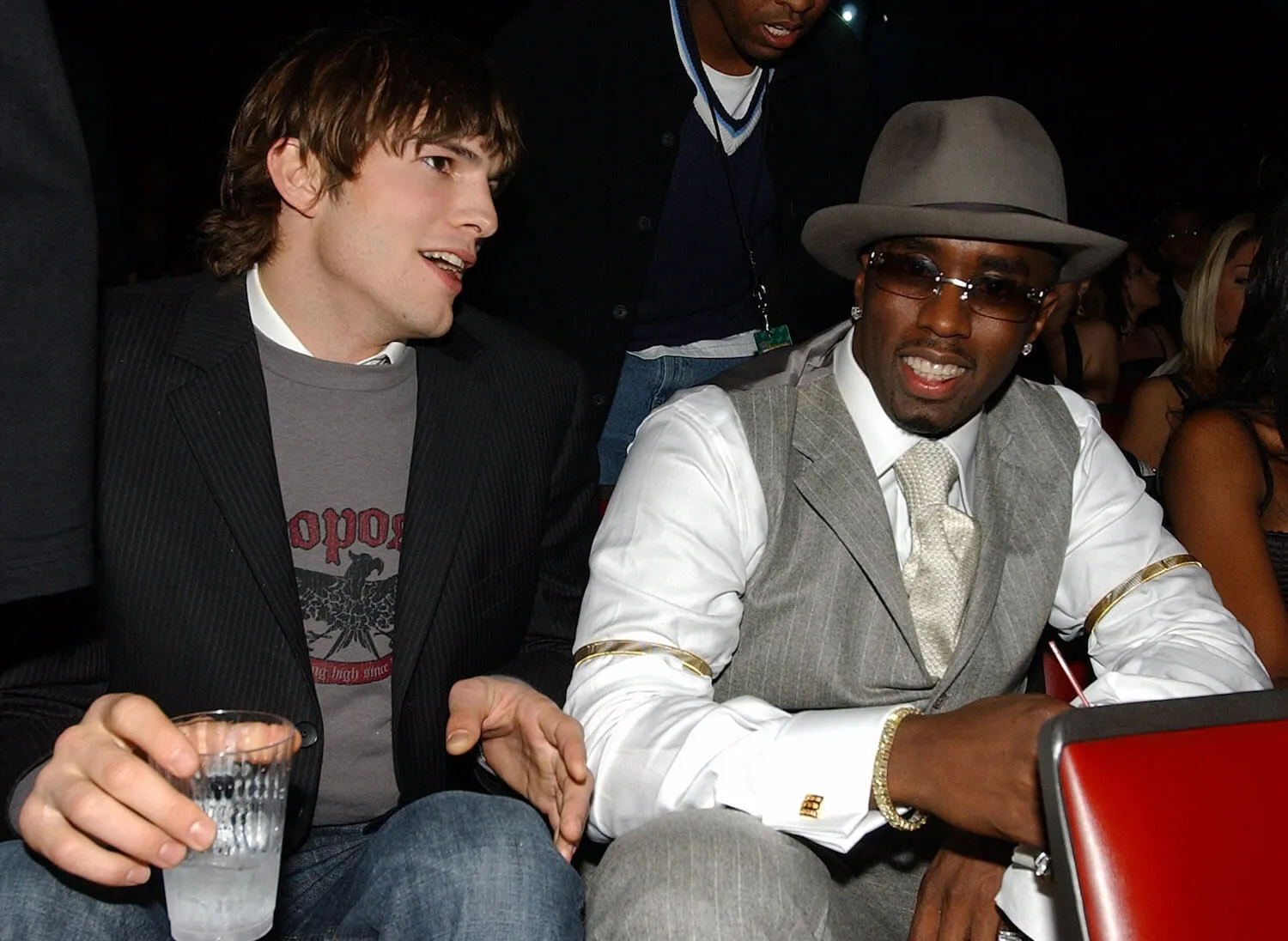 Ashton Kutcher and Sean 'Diddy' Combs sitting next to each other and talking at a VH1 event in 2003