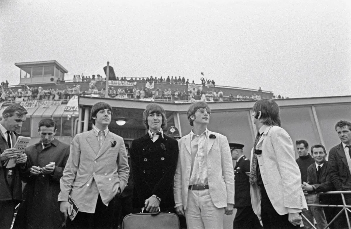 A black and white picture of the Beatles standing at an airport. 