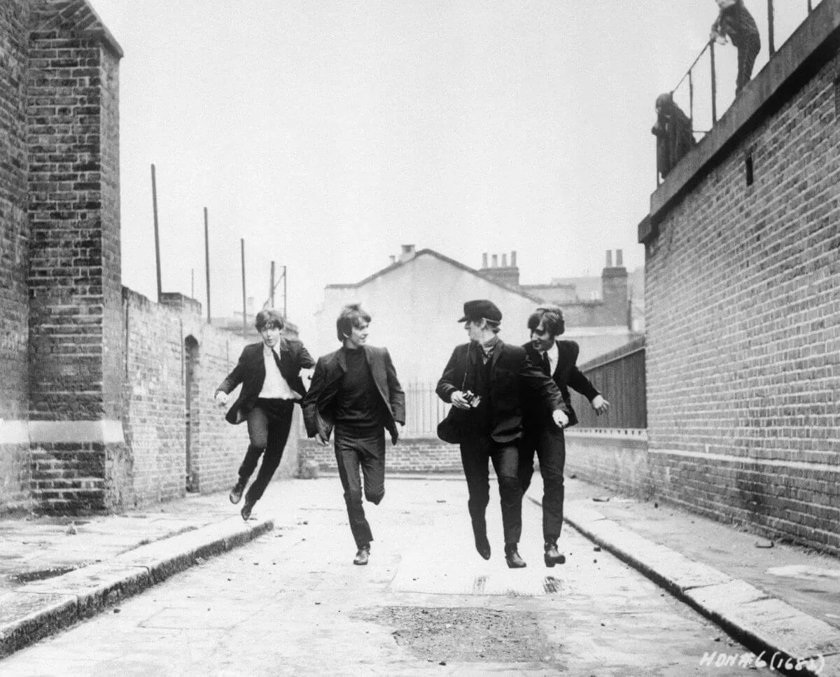 A black and white picture of The Beatles running down an alley.