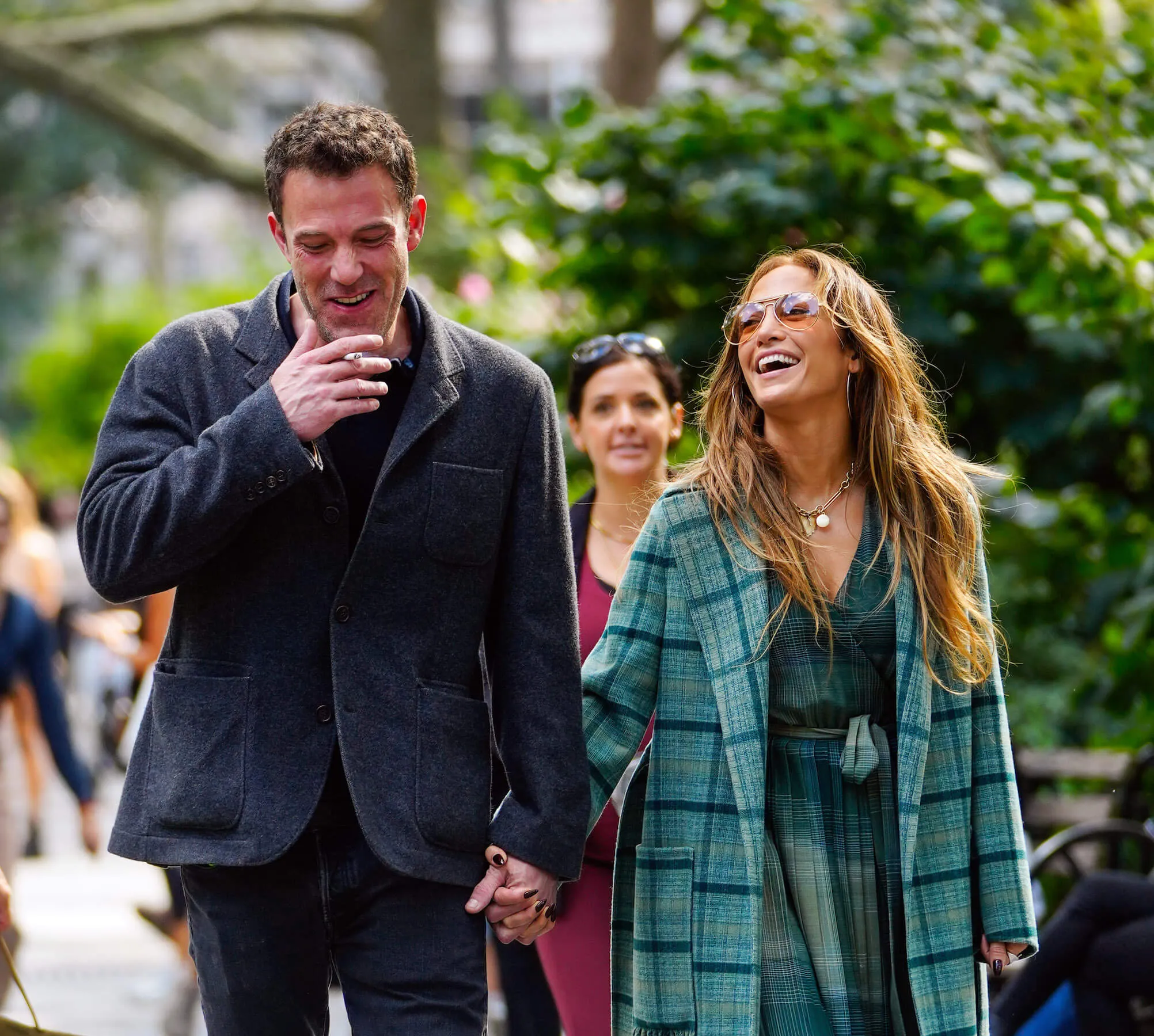 Ben Affleck and Jennifer Lopez walking side by side in New York City. Lopez is wearing a green plaid coat and Affleck is wearing a gray jacket. They're laughing.