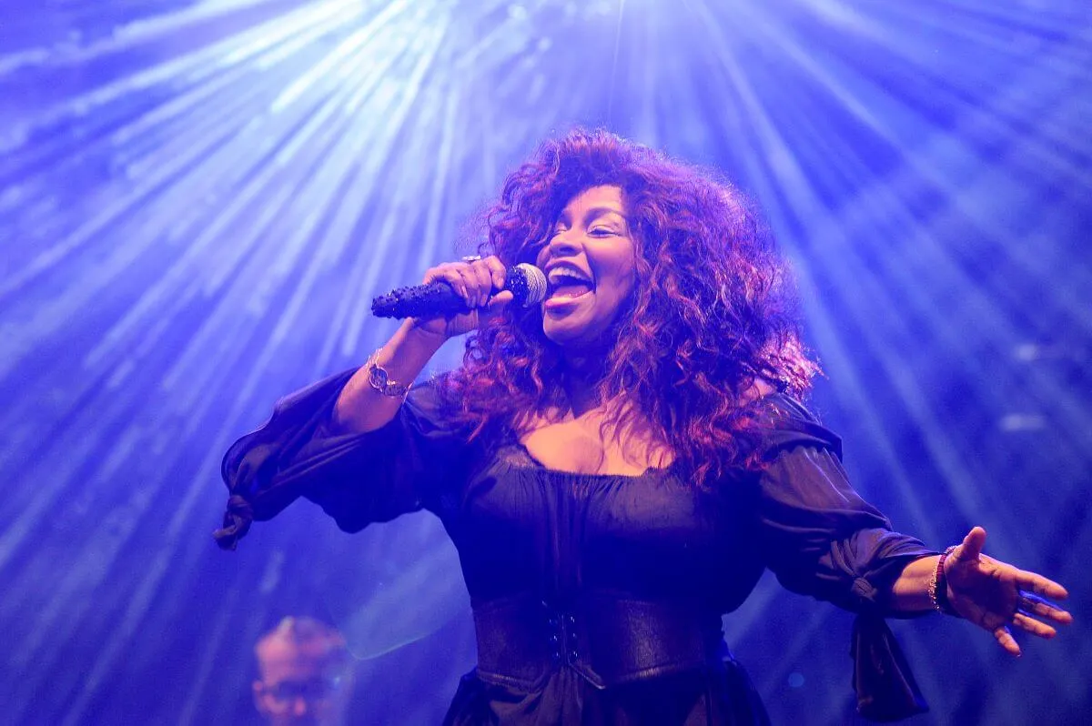 Chaka Khan wears a black dress and sings into a microphone.