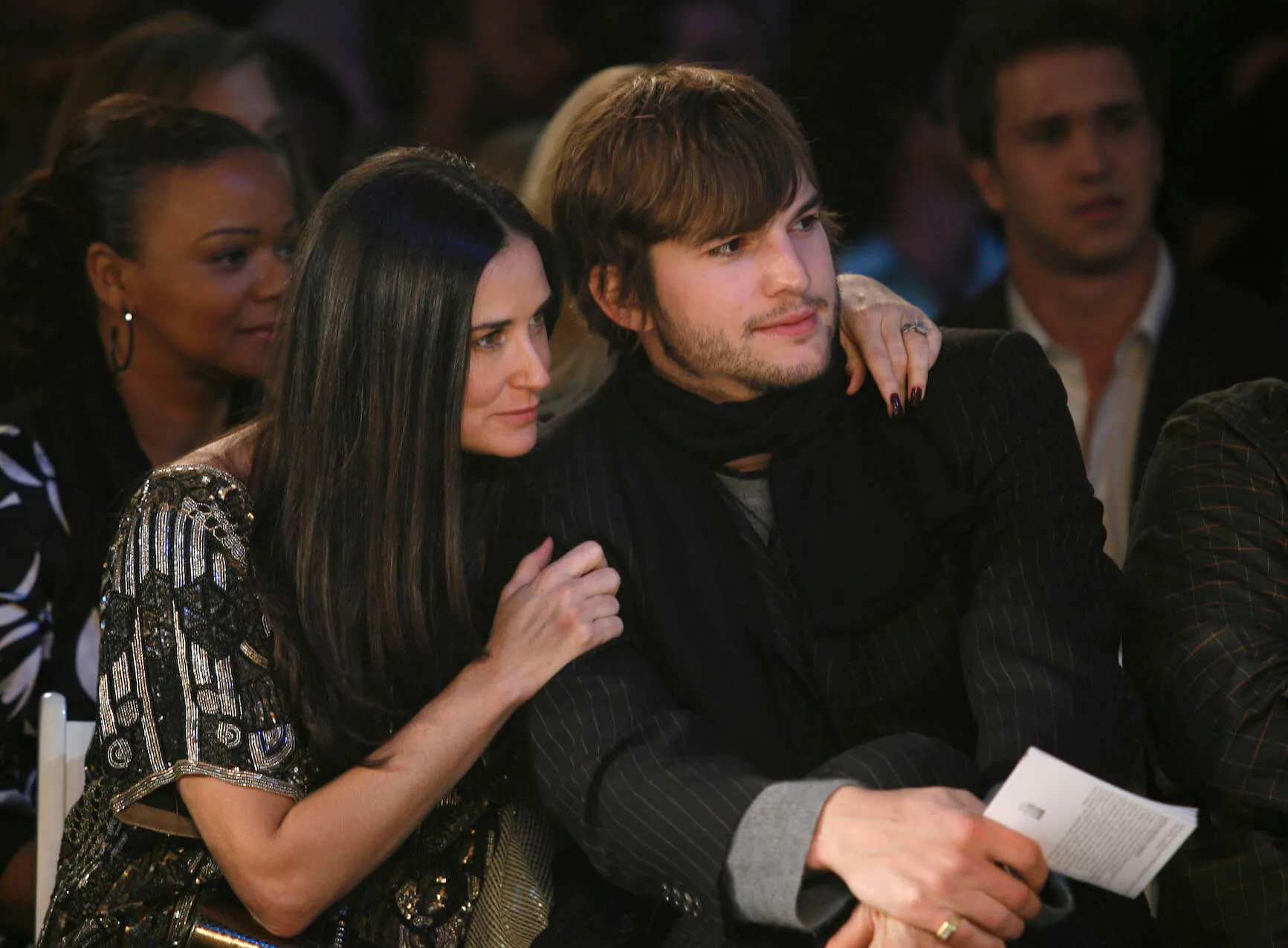 Demi Moore clutching on to Ashton Kutcher's shoulders as they both look off to their left at an event.