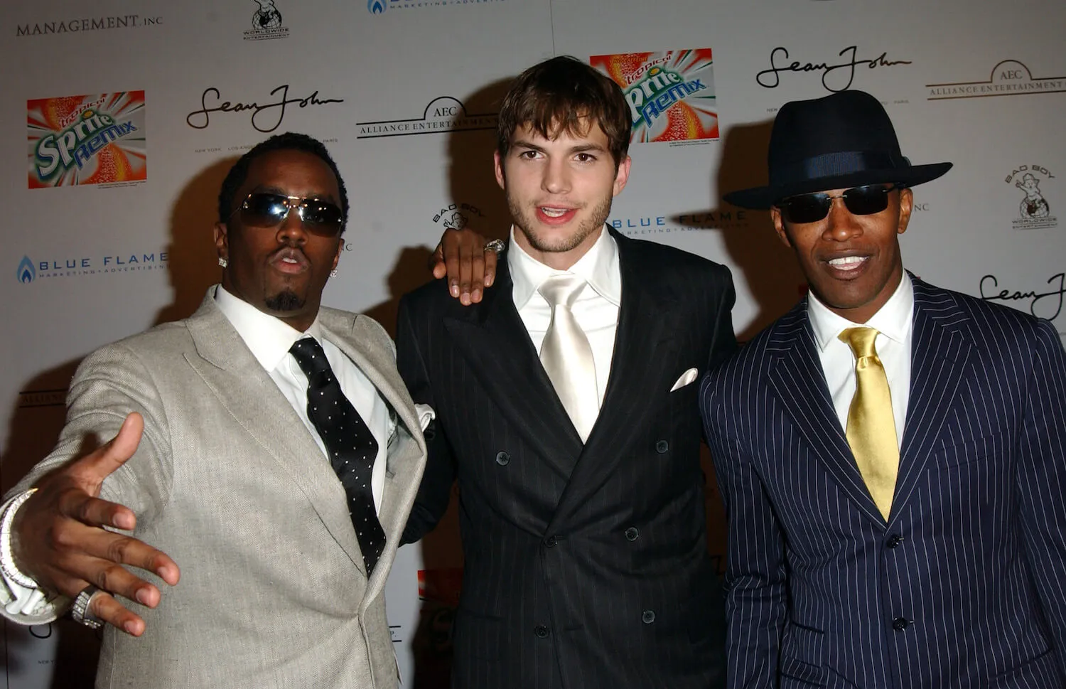 Sean 'Diddy' Combs, Ashton Kutcher, and Jamie Foxx with their arms around each other posing in suits