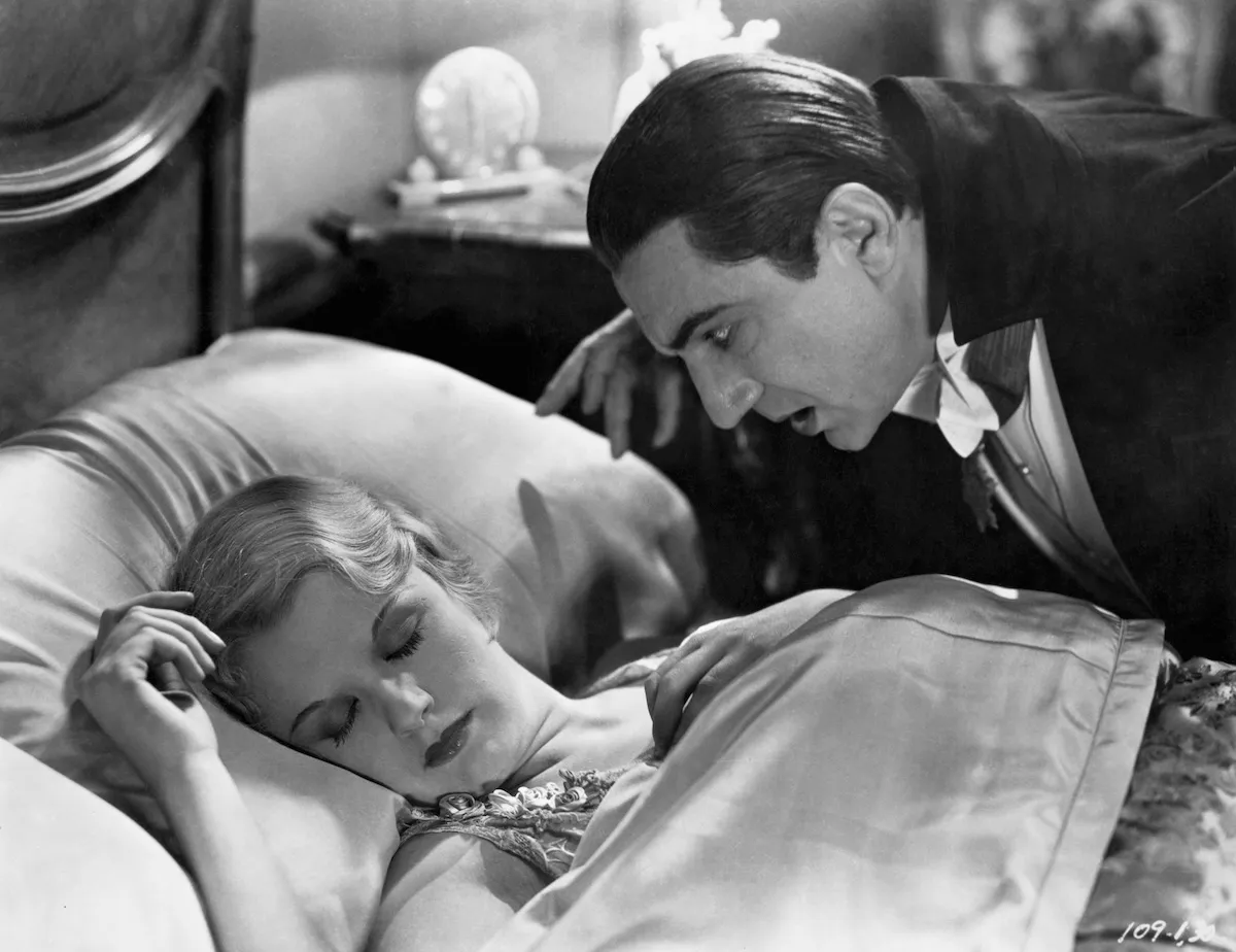 Black and white image of Bela Lugosi as Dracula looming over a sleeping woman