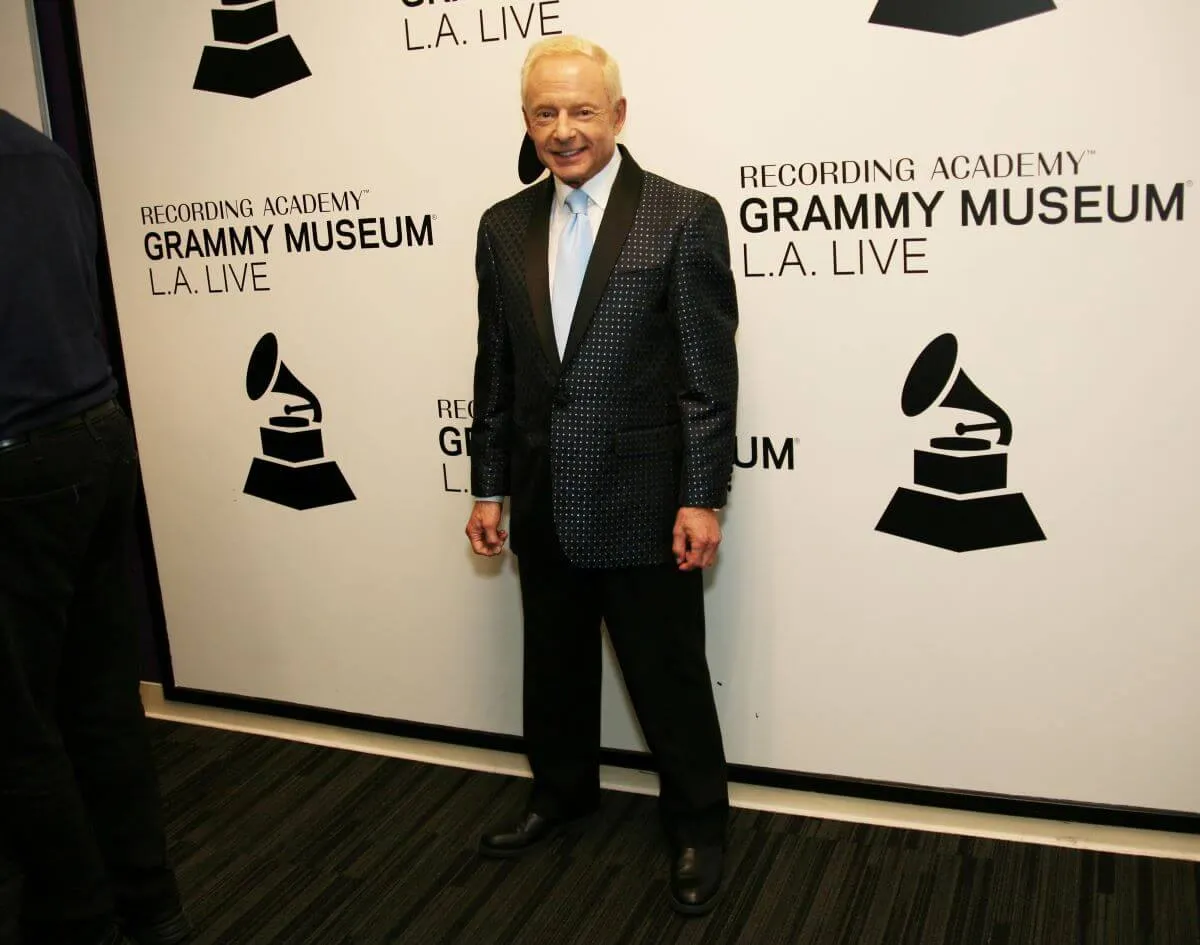 Elliot Mintz wears a black suit and stands in front of a white background.