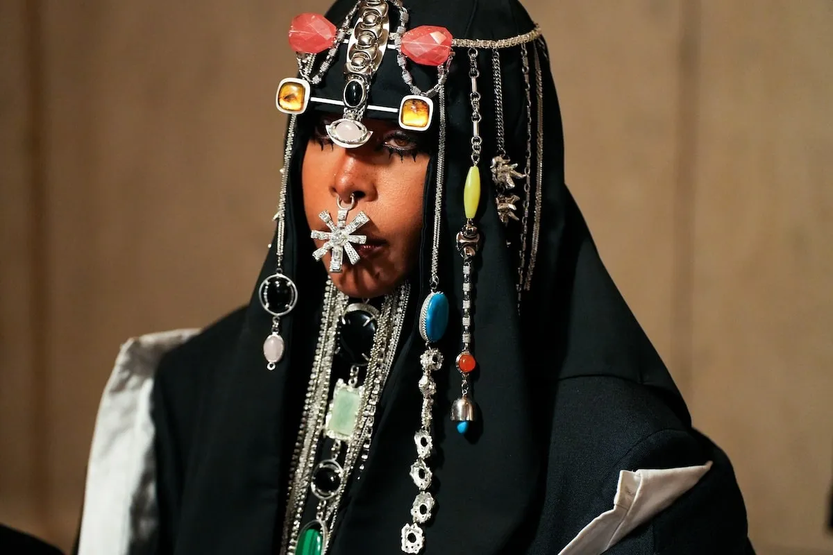 Wearing a black coat, dress, and headpiece, Erykah Badu poses for photos at the CFDA Fashion Awards 2024