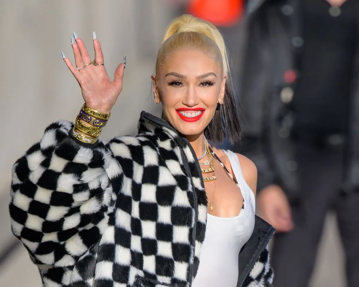 Gwen Stefani wears a black and white checkered jacket. She waves.