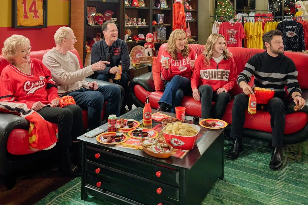 A family wearing Kansas City Chiefs gear and sitting on couches in the Hallmark movie 'Holiday Touchdown: A Chiefs Love Story'