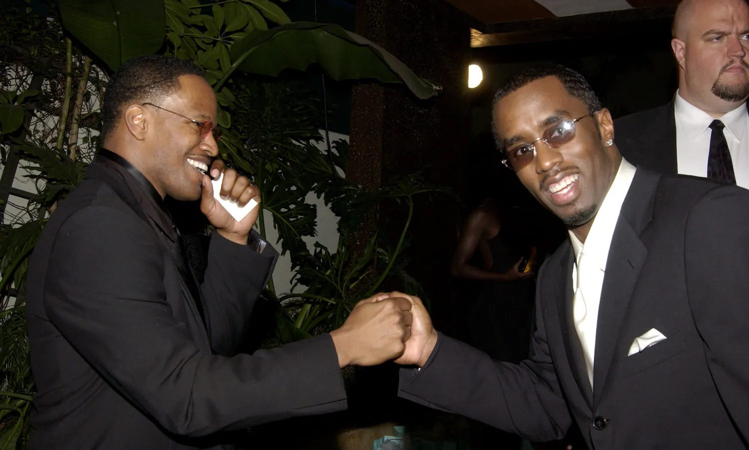 Jamie Foxx and Sean 'Diddy' Combs shaking hands against a dark background